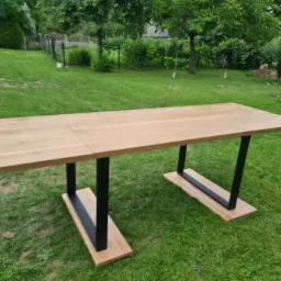 Rozkładany stół z jasnego drewna z czarnymi, metalowymi nogami na trawniku w ogrodzie.