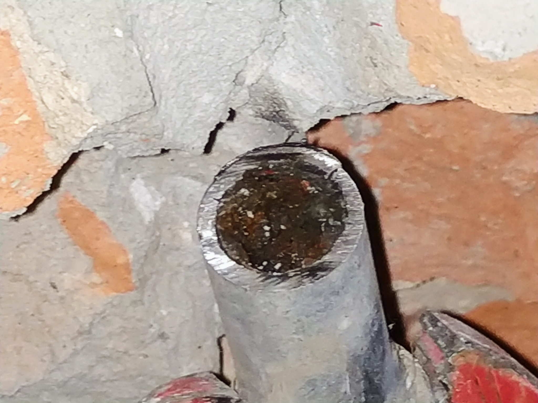 Przekrój skorodowanej, metalowej rury wystającej ze ściany z cegły i betonu. Widoczne ślady rdzy wewnątrz rury.