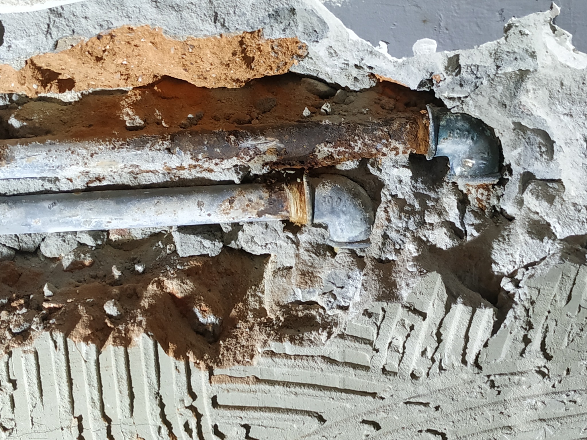Odkryte, zardzewiałe rury grzewcze w ścianie podczas remontu, widoczne ślady po kuciu w tynku i odsłonięta cegła