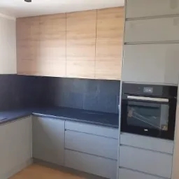 Szare szafki kuchenne z drewnianymi górnymi szafkami i czarnym blatem w kuchni w Gdańsku, widoczny piekarnik.