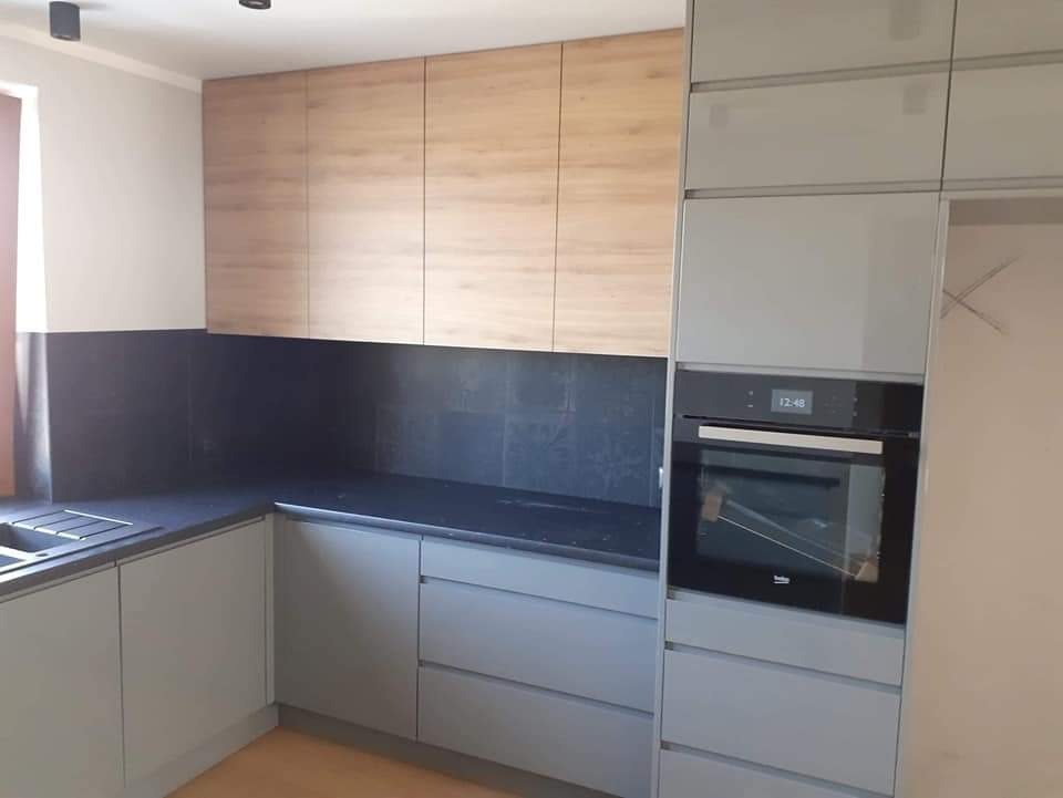 Szare szafki kuchenne z drewnianymi górnymi szafkami i czarnym blatem w kuchni w Gdańsku, widoczny piekarnik.