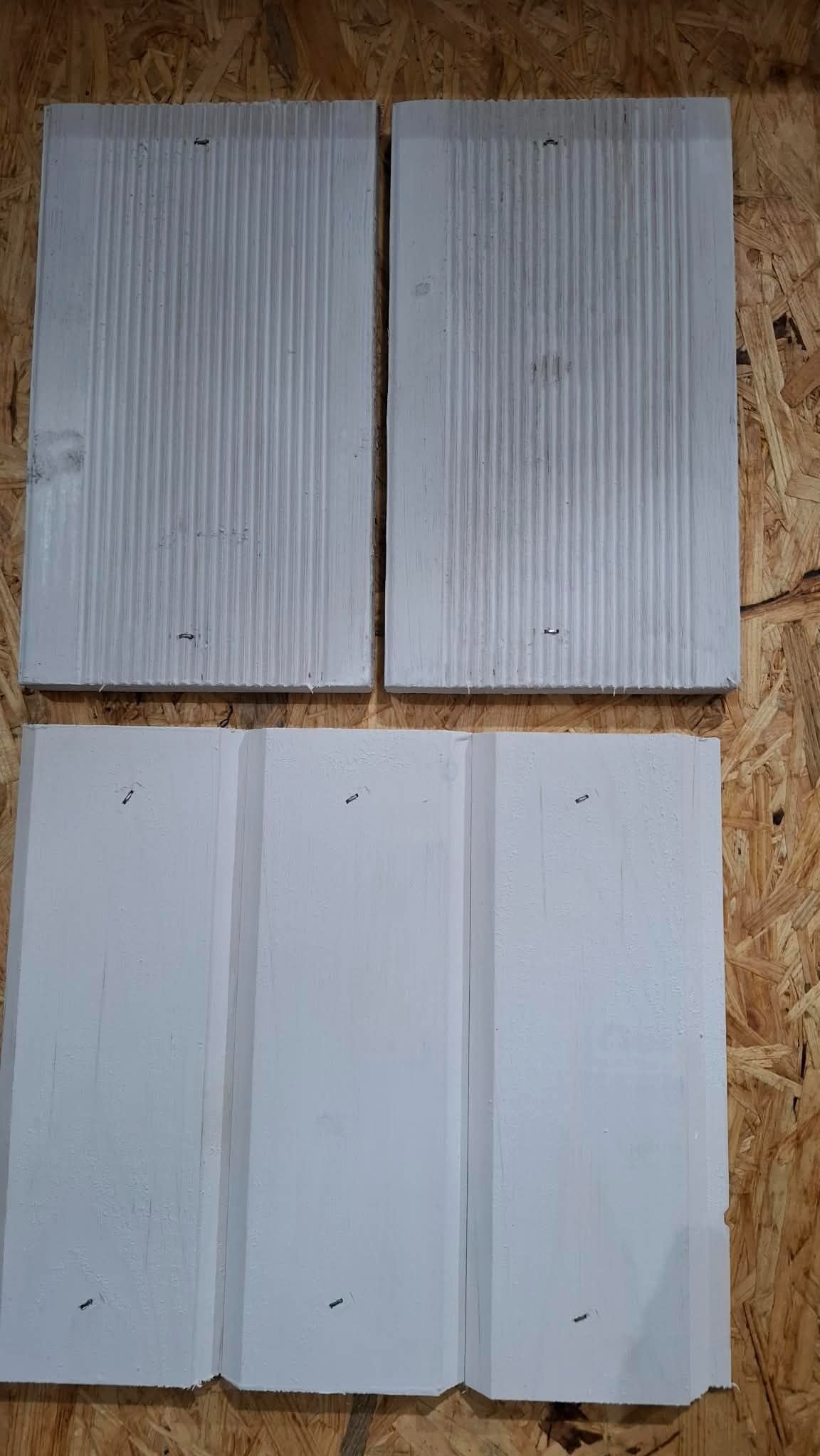Białe, pomalowane deski z rowkami i wypustkami, ułożone na płycie OSB. Dwie deski kwadratowe u góry, trzy deski pionowe u dołu. Widoczne ślady po gwoździach.