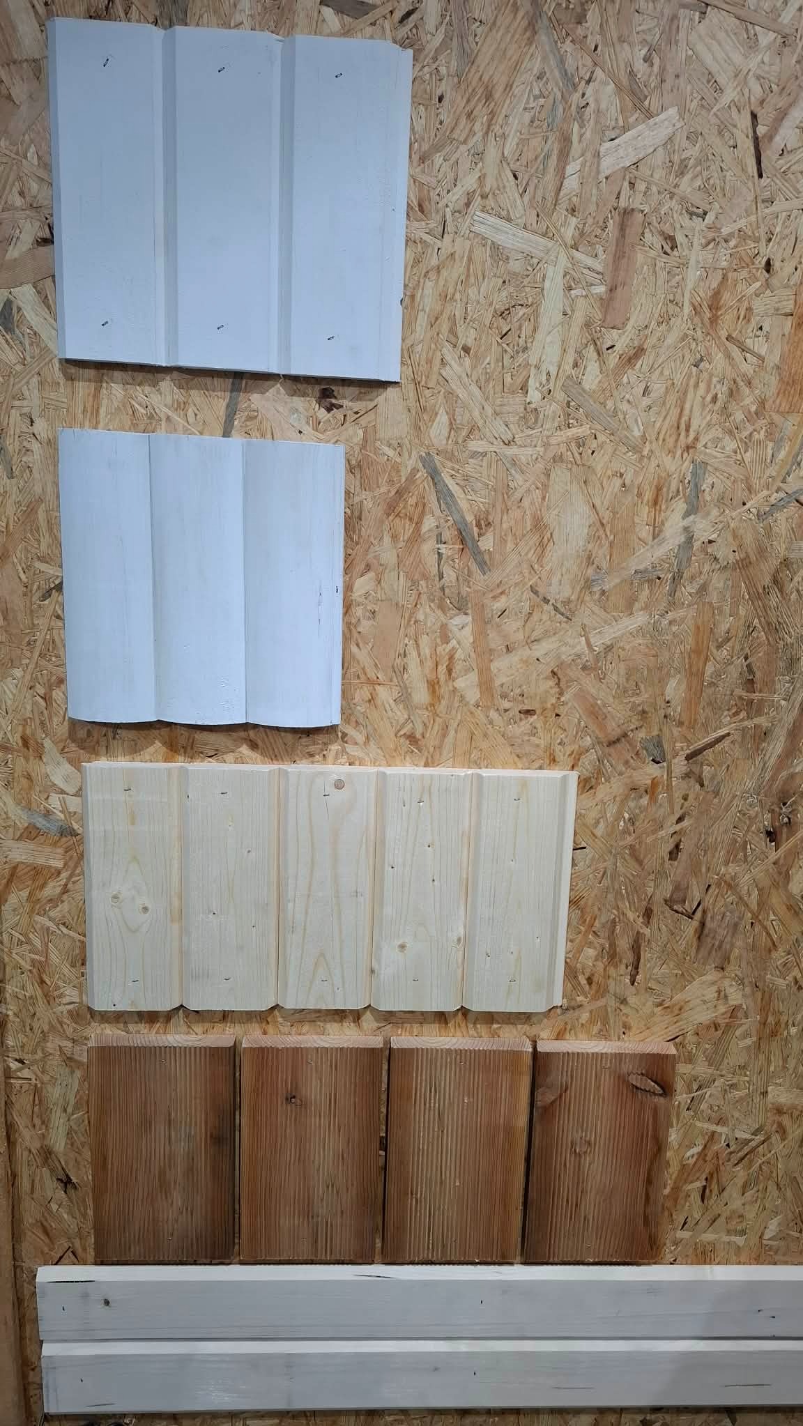 Ekspozycja próbek drewnianych paneli ściennych w różnych kolorach i wzorach, zamocowanych na płycie OSB. Prezentacja wykończeń wnętrz.