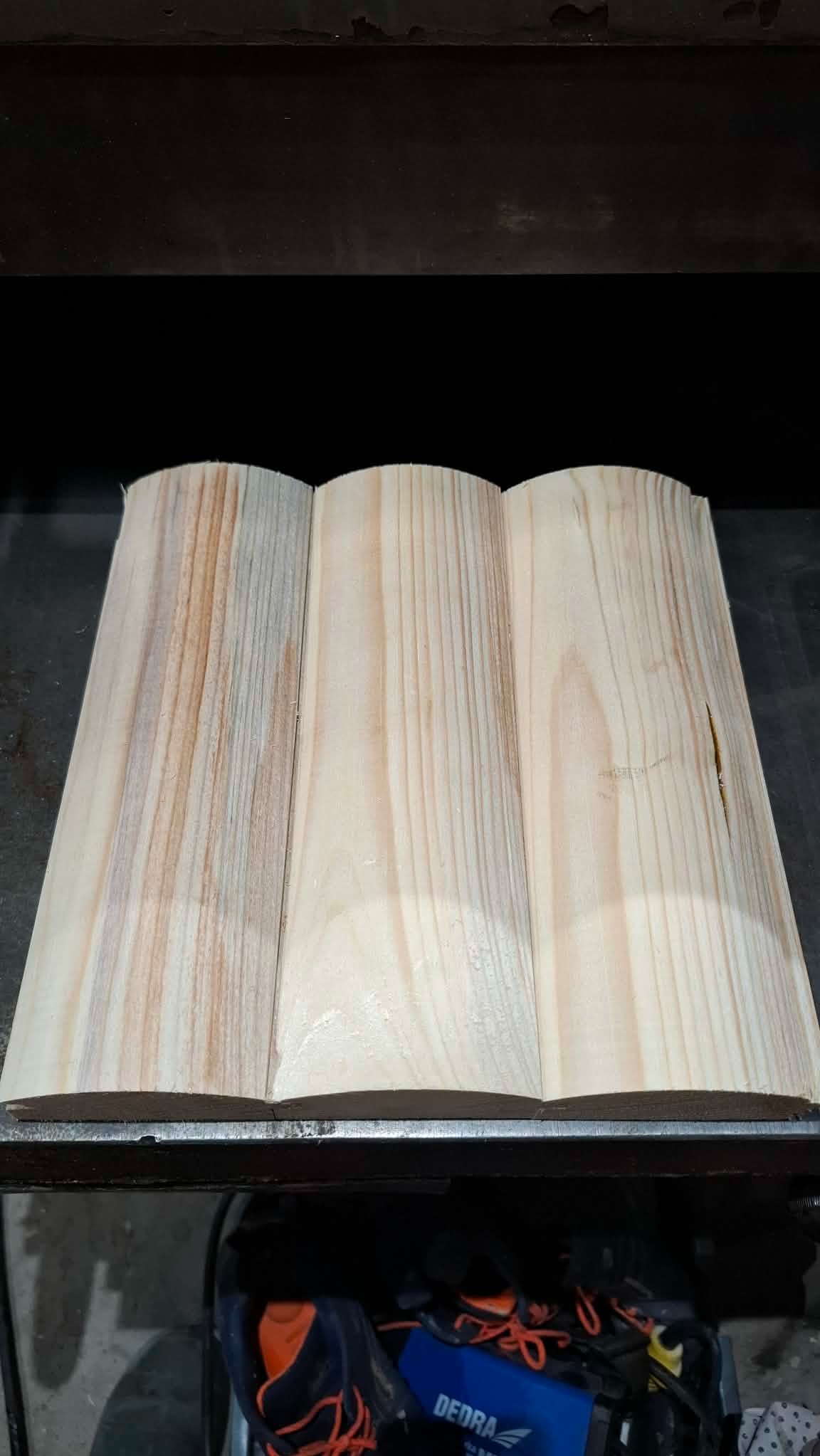 Trzy profilowane deski z jasnego drewna, ułożone obok siebie, ukazujące naturalny rysunek słojów. Widoczne ślady obróbki i delikatne różnice w odcieniach.