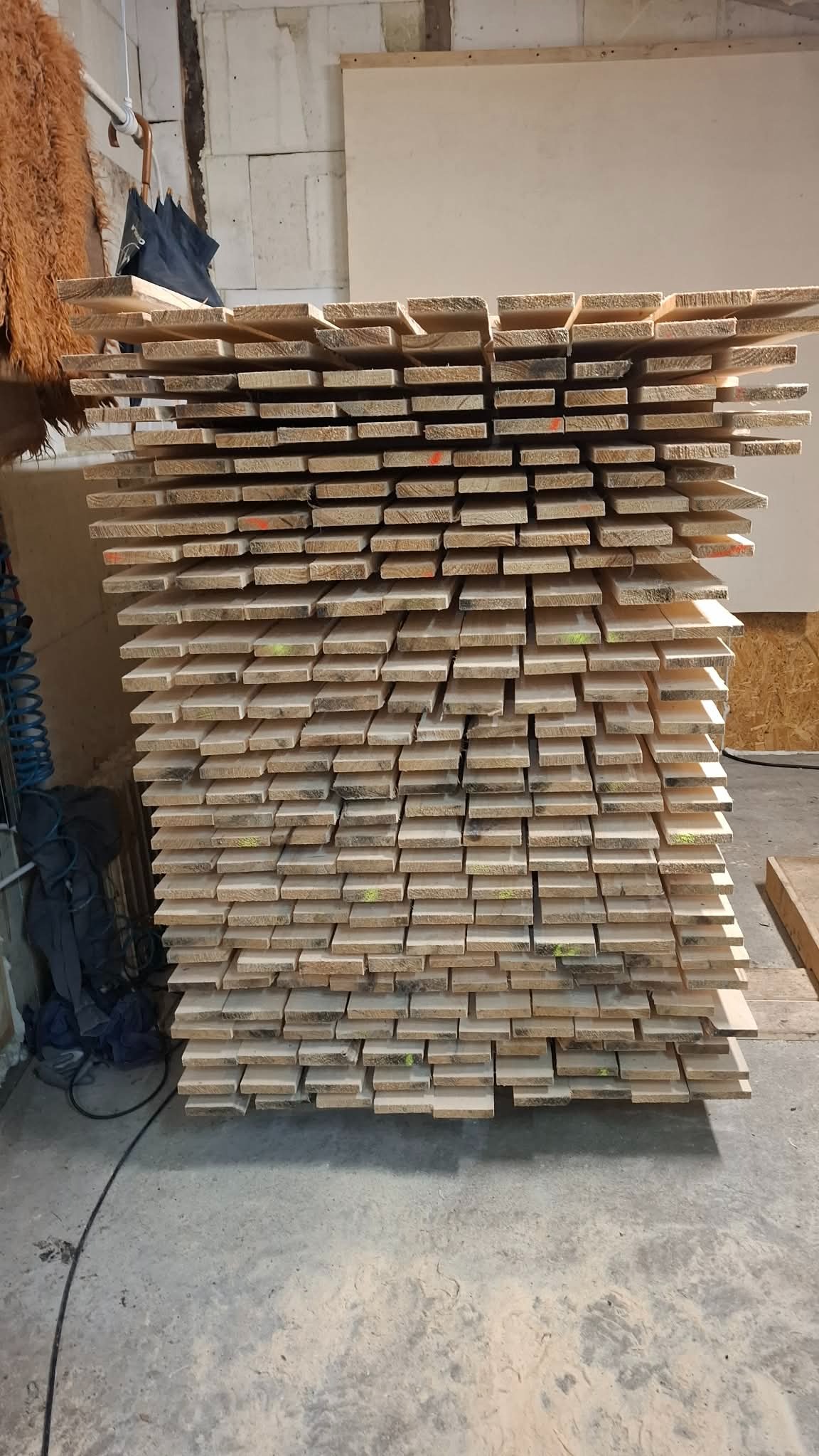 Stos desek z widocznymi oznaczeniami w kolorze pomarańczowym i żółtym, ułożonych równo na sobie. W tle widoczna ściana z betonu komórkowego.