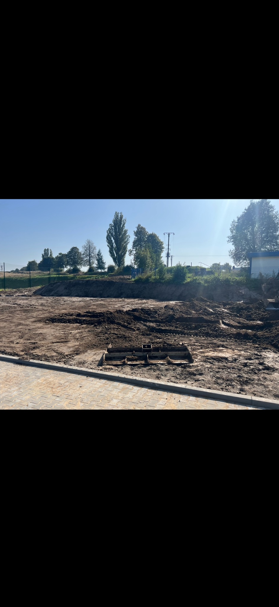 Przygotowany teren pod budowę z częściowo ułożoną kostką brukową na obrzeżach i narzędziem do wyrównywania gruntu w centrum.