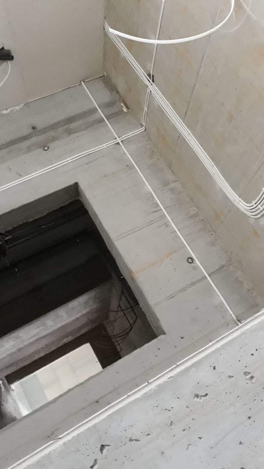 Surowy betonowy strop z otworem i poprowadzonymi białymi kablami elektrycznymi w listwach, widoczne ślady po wierceniu.