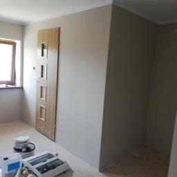 Poezja Team Marcin Gibki - Wnętrze świeżo pomalowanego pokoju z drewnianymi drzwiami z przeszkleniami, widoczne puszki farby i materiały budowlane na podłodze