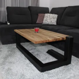 Stolik kawowy z drewnianym blatem i czarną, metalową podstawą w salonie w Nowielicach, na puszystym dywanie w tle ciemna kanapa z poduszkami.