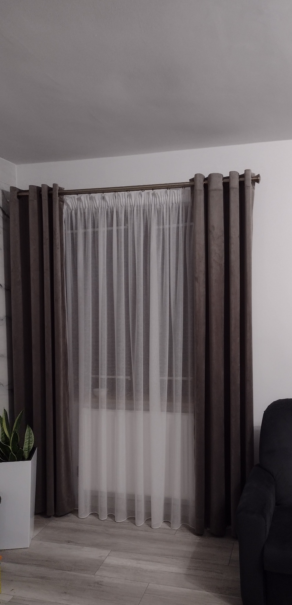 Zestawienie: beżowe, grube zasłony z metalowymi przelotkami i delikatna, biała firanka. Całość zawieszona na metalowym karniszu. U dołu widoczny fragment szarej podłogi.