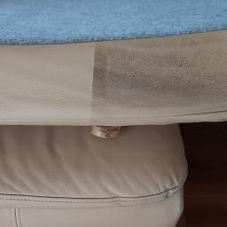 Clean Tom - Fragment beżowej skórzanej kanapy z widoczną różnicą w czystości: po lewej stronie wyczyszczona, po prawej zabrudzona. Na górze leży niebieski koc. Widoczny zamek błyskawiczny i drewniana nóżka.