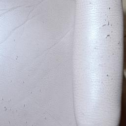 Clean Tom - Fragment beżowego fotela z drewnianym, lakierowanym podłokietnikiem zdobionym srebrnymi nitami, widoczne drobne uszkodzenia tapicerki.