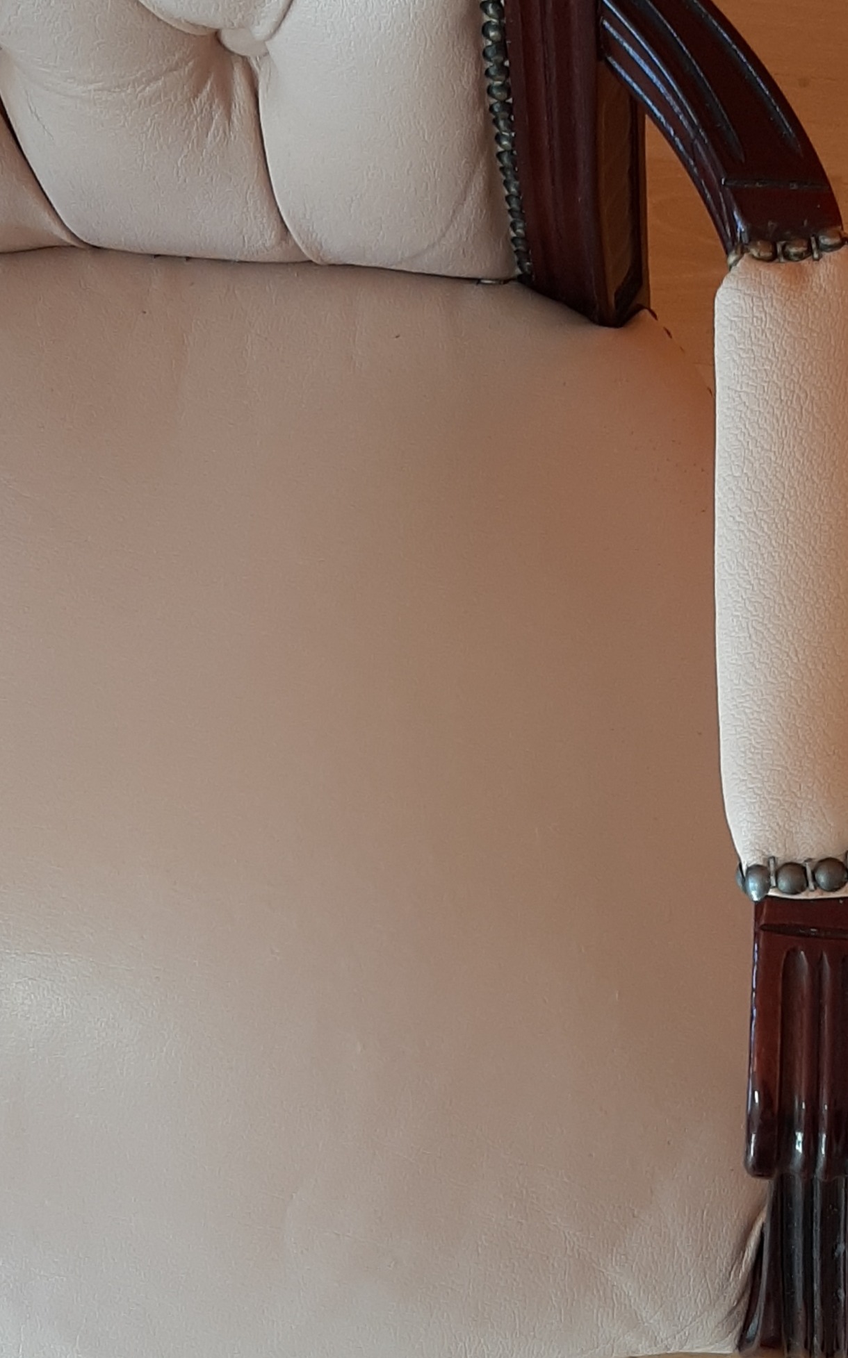 Fragment beżowego fotela z drewnianymi, ciemnobrązowymi zdobieniami i metalowymi ćwiekami, prezentowany w Żyrardowie.