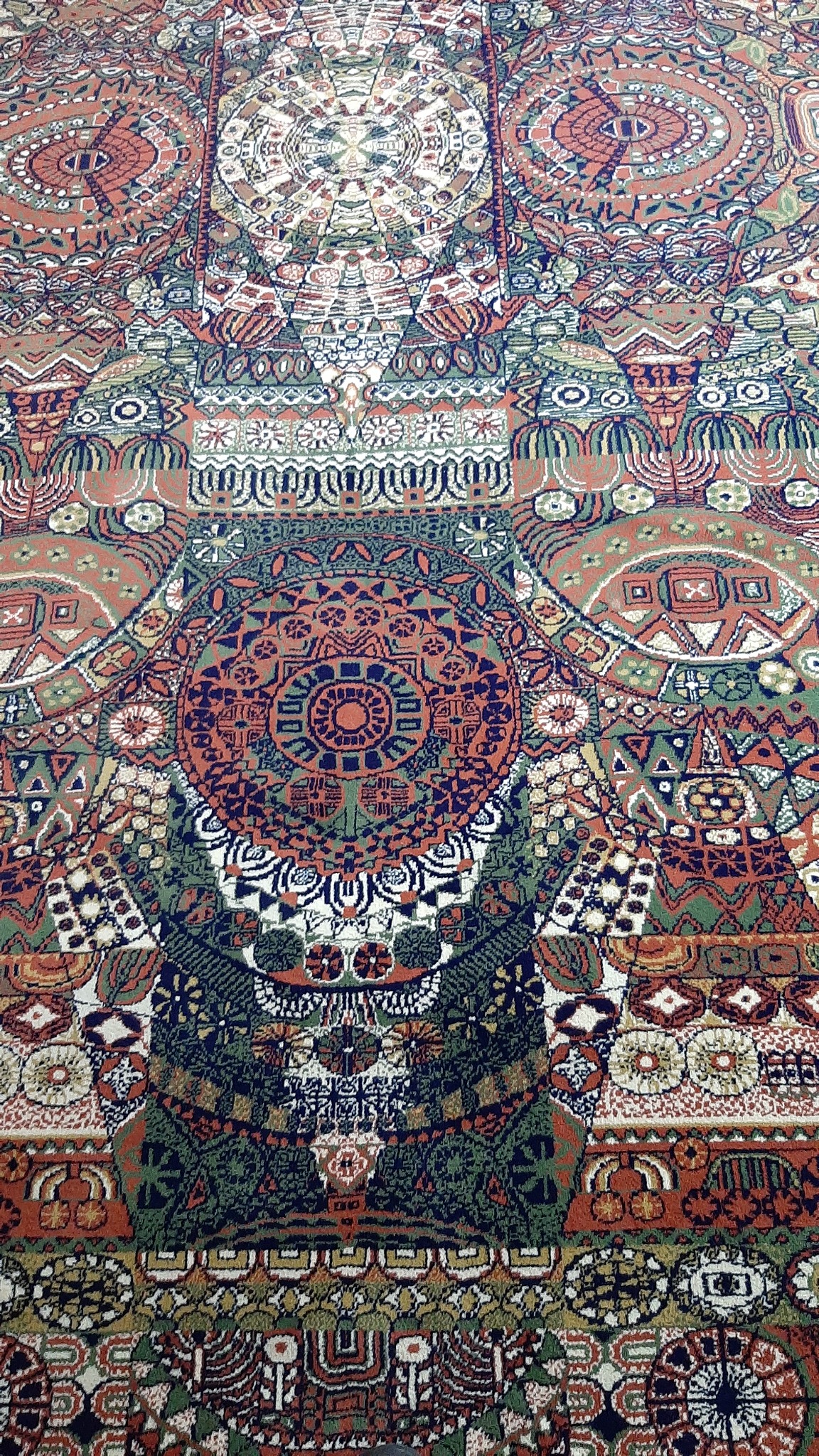 Wzorzysty dywan w odcieniach czerwieni, zieleni i granatu z motywami geometrycznymi i roślinnymi, widoczny z góry.