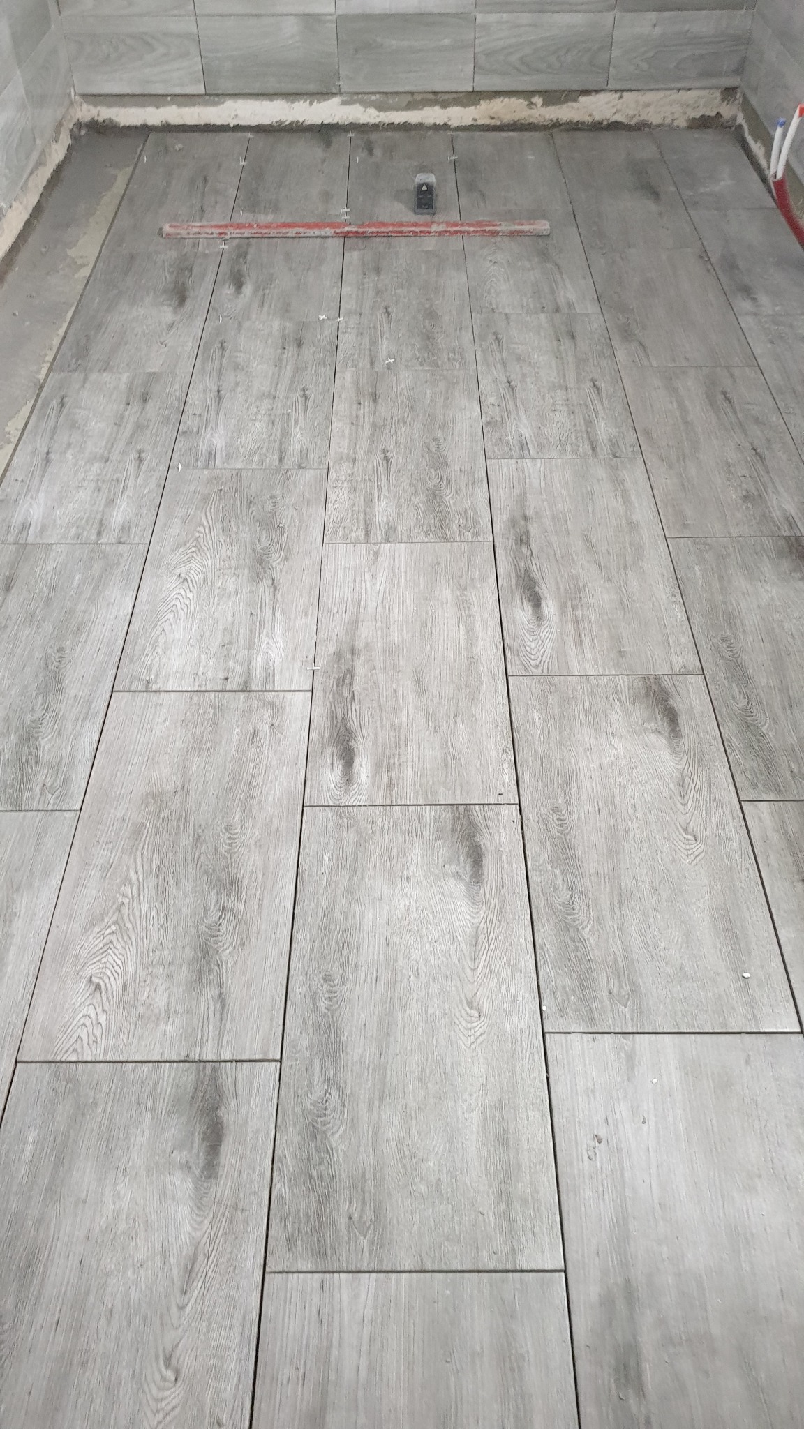 Układanie szarych płytek podłogowych imitujących drewno, z widoczną poziomicą i krzyżykami dystansowymi, na etapie prac w łazience.