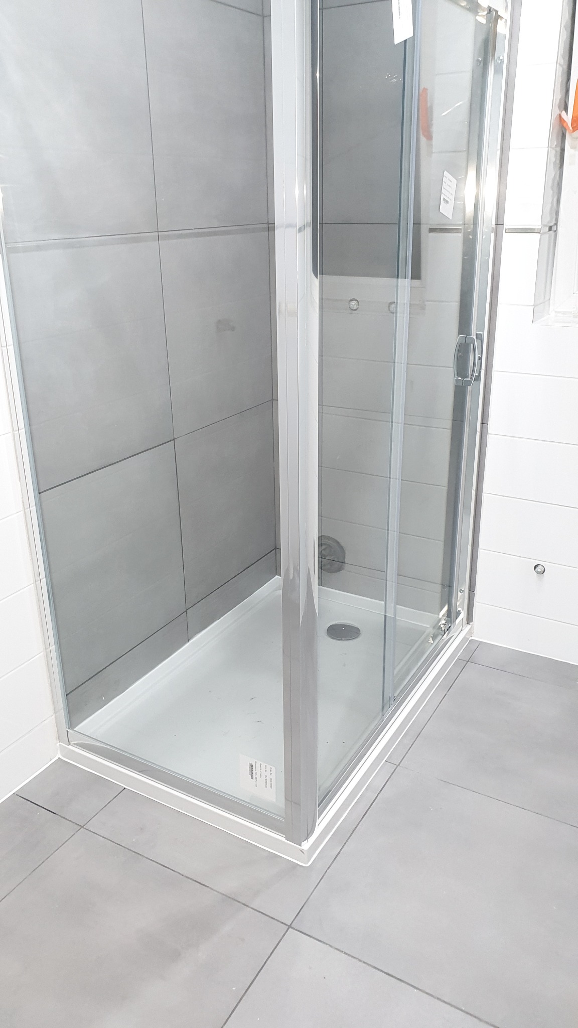 Kabina prysznicowa z przesuwnymi drzwiami, obłożona szarymi, kwadratowymi płytkami na ścianie i podłodze, z widocznym odpływem liniowym.