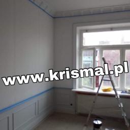 KRISMAL Krzysztof Bąkowski - Pokój przed malowaniem: ściany zabezpieczone niebieską taśmą malarską, widoczna drabina, puszki z farbą i listwy przypodłogowe.