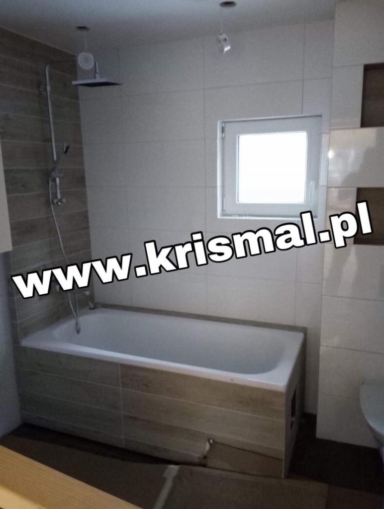 Nowoczesna wanna obudowana płytkami imitującymi drewno, białe płytki na ścianach, kabina prysznicowa typu deszczownica, okno w łazience w Kiszkowie.