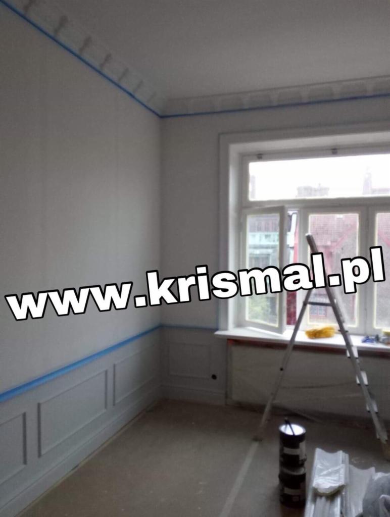 Pokój przed malowaniem: ściany zabezpieczone niebieską taśmą malarską, widoczna drabina, puszki z farbą i listwy przypodłogowe.