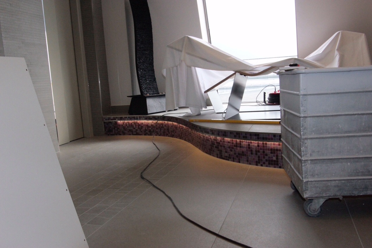 Łazienka w trakcie remontu: widoczna mozaika na zaokrąglonej ścianie, podświetlenie LED, przykryte folią elementy i narzędzia budowlane.