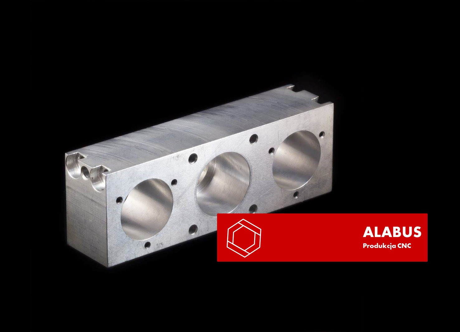 Metalowy blok z trzema otworami, wykonany metodą CNC, oświetlony studyjnie na czarnym tle, z widocznym logo firmy Alabus Produkcja CNC.
