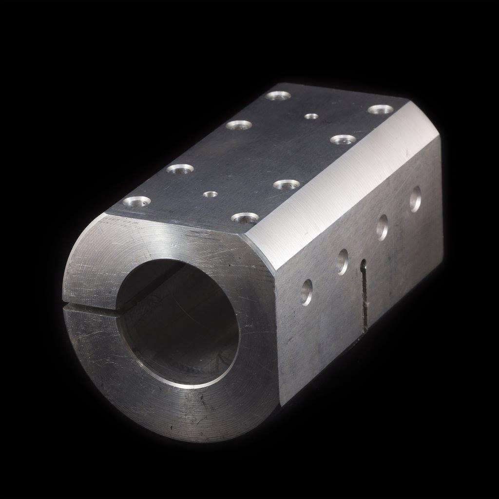 Precyzyjnie obrobiony, aluminiowy element z otworem centralnym i licznymi nawierceniami, sfotografowany na czarnym tle.