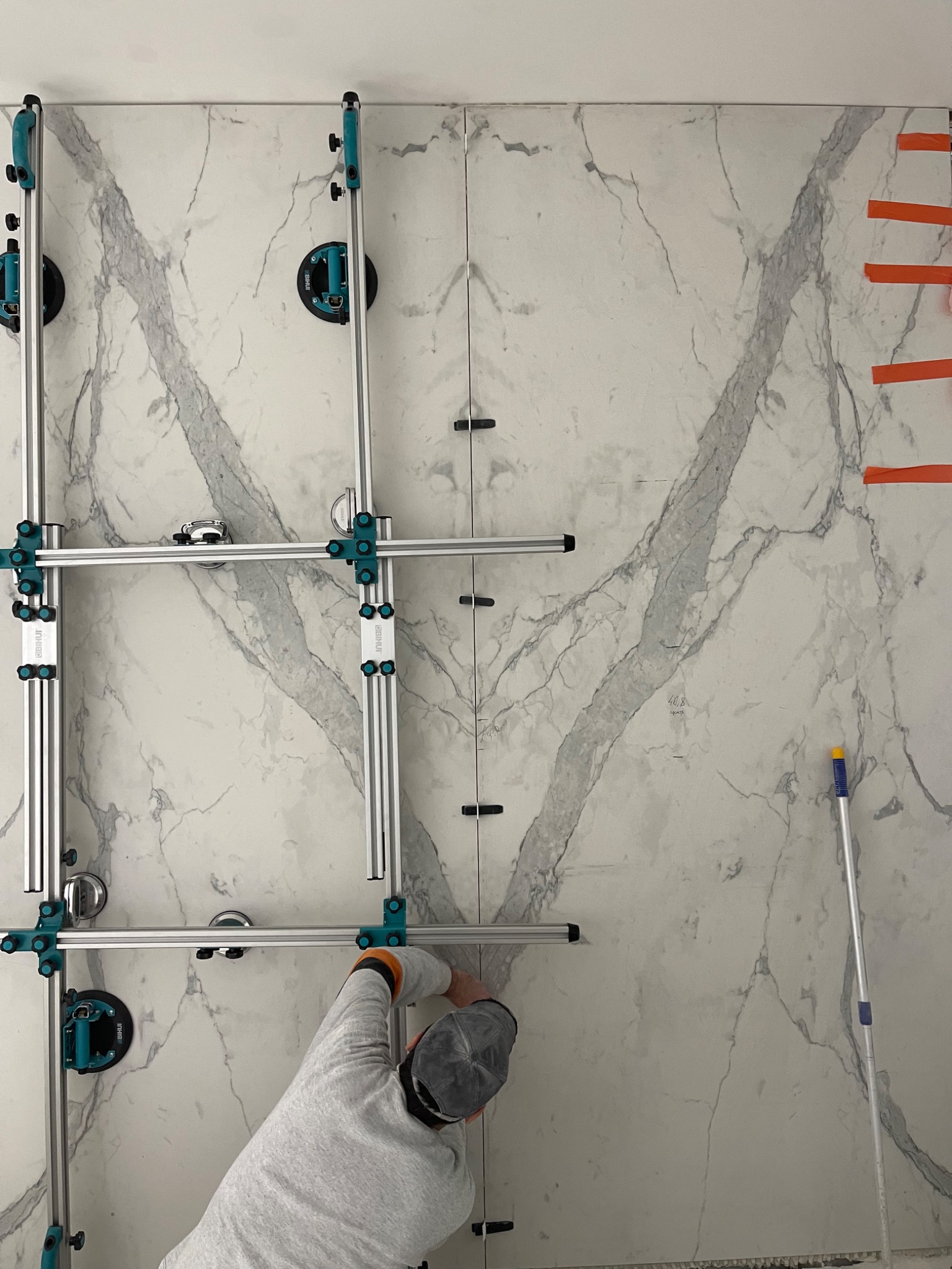 Układanie wielkoformatowych płytek imitujących marmur na ścianie, z użyciem specjalistycznego sprzętu montażowego z przyssawkami i poziomowaniem.