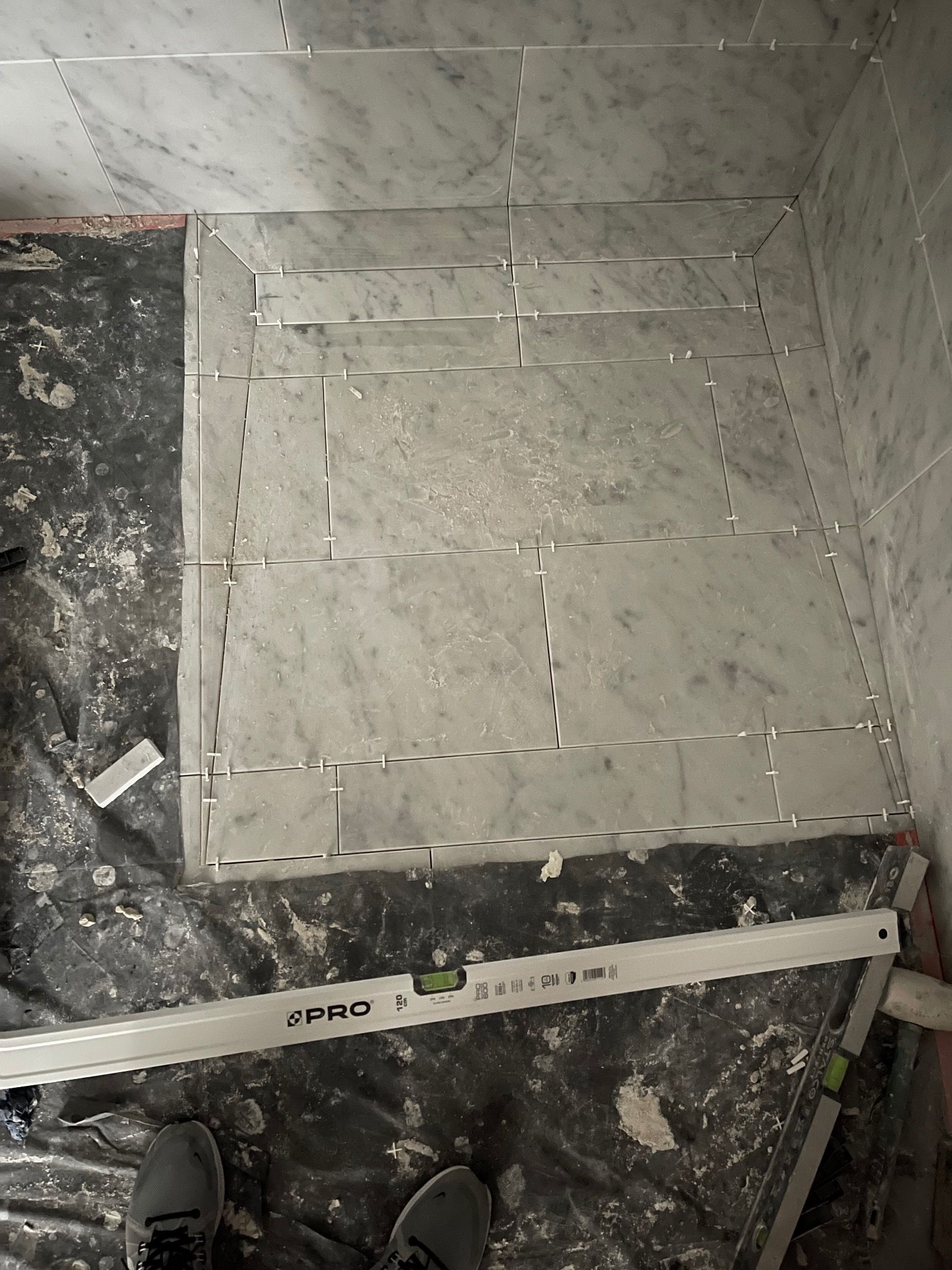 Układanie marmurowych płytek w narożniku pomieszczenia, widoczne poziomice i krzyżyki dystansowe, podłoga zabezpieczona folią.