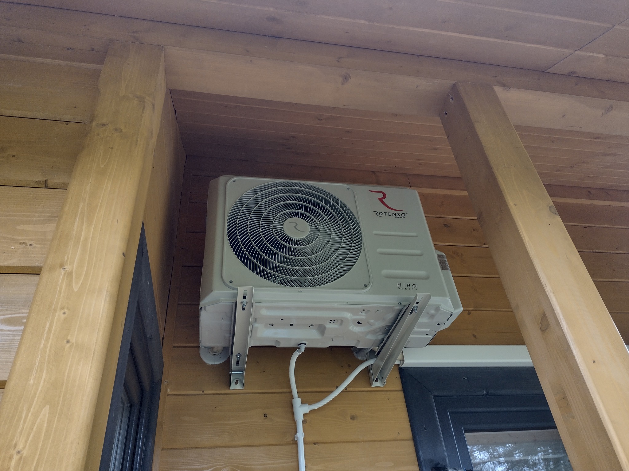 Zamontowany na drewnianej ścianie zewnętrzny moduł klimatyzatora Rotenso w Masłońskim, widoczne mocowania i instalacja odprowadzająca skropliny.