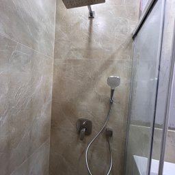 DDK PROF - Beżowa kabina prysznicowa z deszczownicą i słuchawką, wykończona płytkami imitującymi marmur, z widocznym fragmentem wanny.