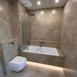 DDK PROF - Beżowa łazienka z podświetleniem LED, wiszącą toaletą i wanną z parawanem nawannowym, wykończona marmurowymi płytkami.