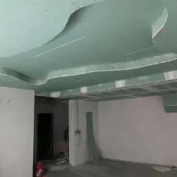 Niedokończony sufit podwieszany z płyty gipsowo-kartonowej z dekoracyjnymi wycięciami, widoczne przewody elektryczne i puszka farby w surowym wnętrzu.