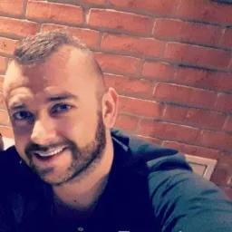 Portret uśmiechniętego mężczyzny z brodą na tle ściany z czerwonej cegły w Bolszewie.