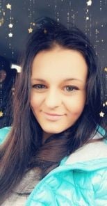 Portret uśmiechniętej kobiety z długimi, ciemnymi włosami, w turkusowej kurtce puchowej, z delikatnym makijażem i błyszczącymi efektami na zdjęciu.