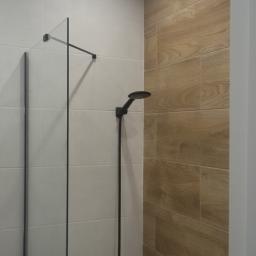 Marcin Modzelewski - Nowoczesna kabina prysznicowa z czarną armaturą i dwoma rodzajami płytek: białymi oraz imitującymi drewno, podświetlona punktowym światłem.