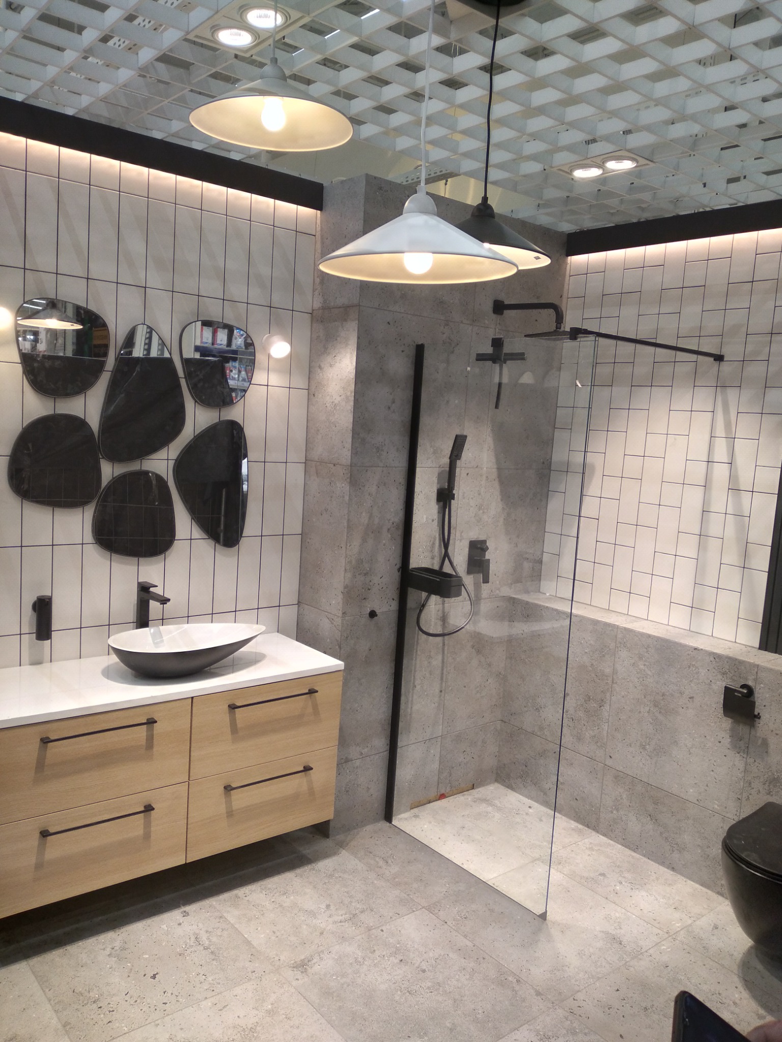 Nowoczesna łazienka z kabiną prysznicową, umywalką nablatową i zestawem luster o organicznych kształtach na ścianie z białych płytek.