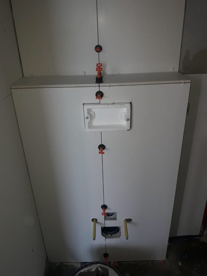 Stelaż podtynkowy do WC w trakcie montażu, z widocznymi elementami poziomowania płytek i wyprowadzonymi rurami przyłączeniowymi.