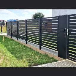 Nowoczesne ogrodzenie panelowe w kolorze czarnym z poziomymi szczeblami i furtką z zamkiem, trawnik z przodu.