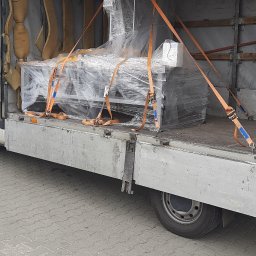 Usługi Transportowe Robert Kołodziejski - Maszyna przemysłowa owinięta folią stretch, zabezpieczona pomarańczowymi pasami transportowymi w przestrzeni ładunkowej busa z plandeką.