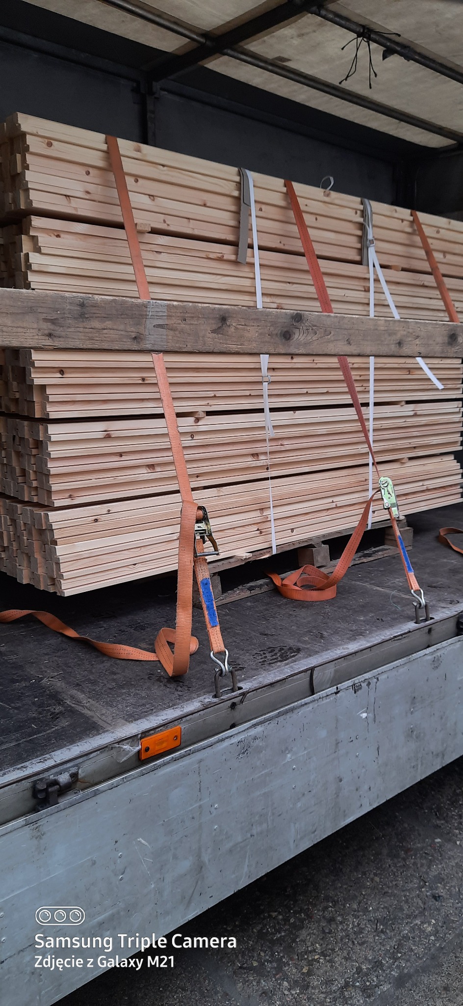 Stos desek zabezpieczony pasami transportowymi wewnątrz skrzyni ładunkowej pojazdu.