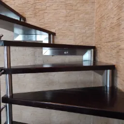 Spiralne schody z ciemnego drewna z metalowymi wspornikami, widok z dołu, ściana wykończona dekoracyjną cegłą.