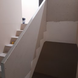 Adam Wiśniewski - Montaż obudowy schodów z płyt gipsowo-kartonowych, widoczne metalowe profile i poziomica na schodach, surowe wykończenie.