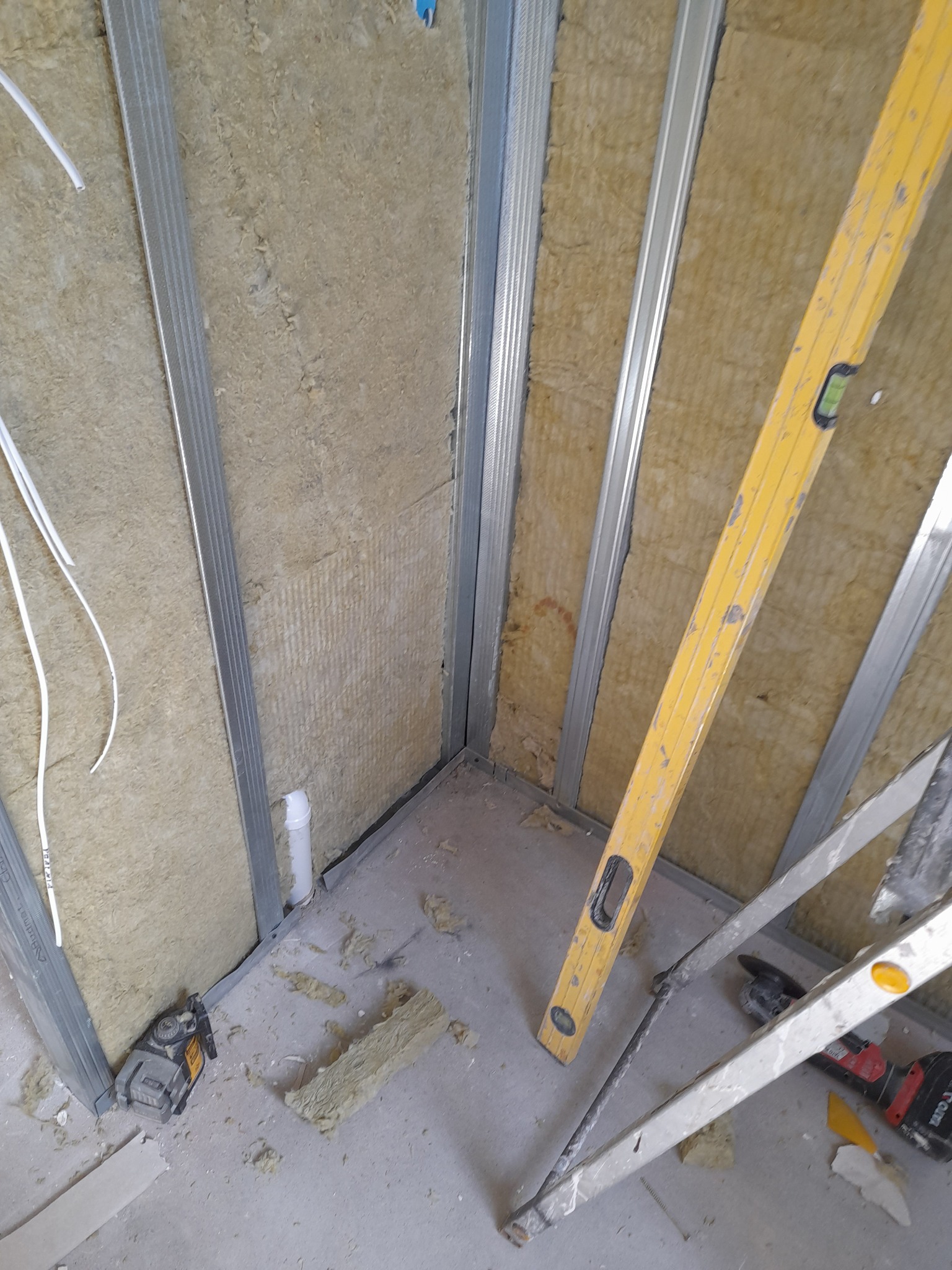 Montaż izolacji z wełny mineralnej w metalowym stelażu, widoczna poziomica, drabina i laser krzyżowy.