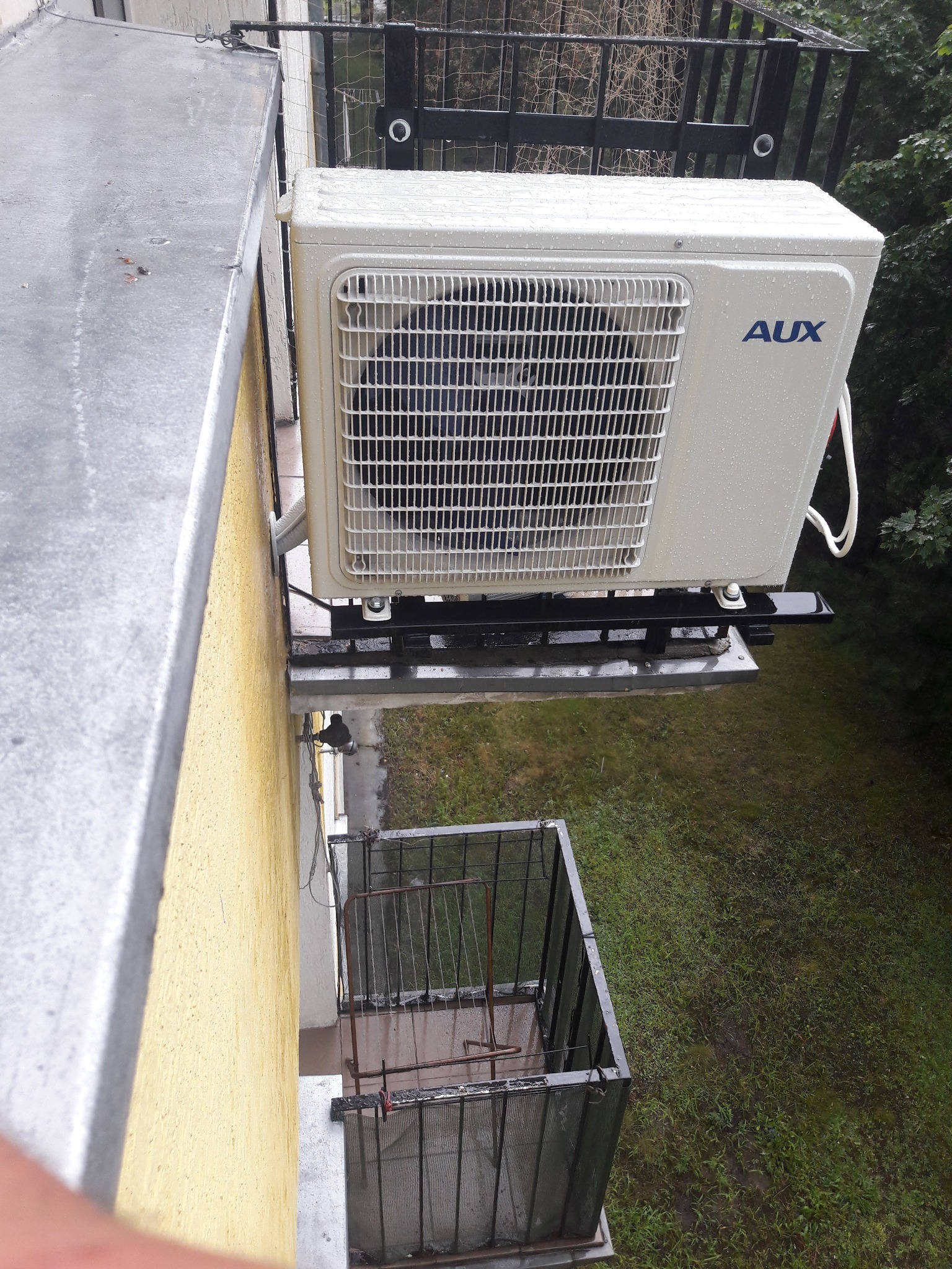 Zewnętrzna jednostka klimatyzacji AUX zamontowana na balkonie w deszczowy dzień, widok z góry.