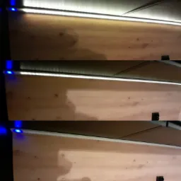 Niedokończona ściana z płyt OSB oświetlona listwą LED z niebieską diodą na krawędzi.