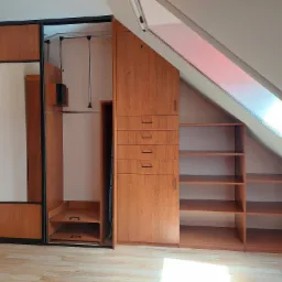 Drewniana szafa wnękowa z przesuwnymi drzwiami i lustrem, dopasowana do skosu poddasza, z wysuwanymi półkami i drążkami na ubrania.