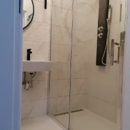 Nowoczesna łazienka z kabiną prysznicową typu walk-in, panelem natryskowym z hydromasażem i umywalką nablatową z czarną armaturą, wykończona płytkami w geometryczny wzór.