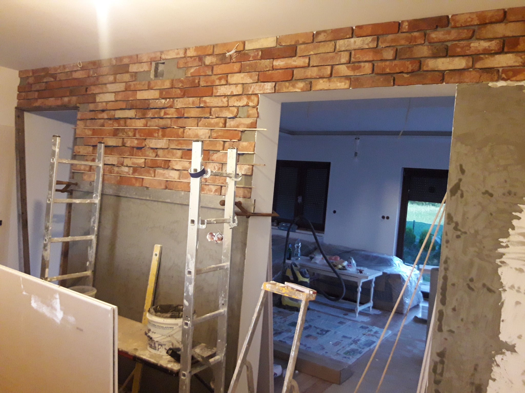 Montaż dekoracyjnej ściany z cegły w trakcie remontu mieszkania, widoczne rusztowania i materiały budowlane.