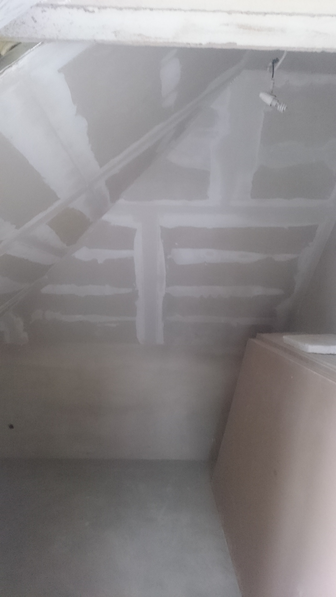 Wnętrze poddasza z zamontowaną płytą kartonowo-gipsową na skosach i suficie, widoczne pasy łączeń przed szpachlowaniem, surowy beton na podłodze, tymczasowe oświetlenie.