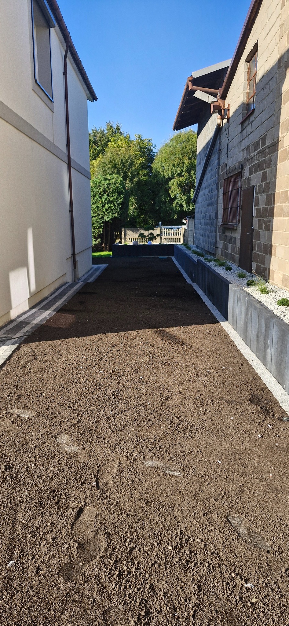 Przygotowany teren pod trawnik lub ogród, ziemia wyrównana, obrzeża z kostki, widok z góry, słoneczny dzień.